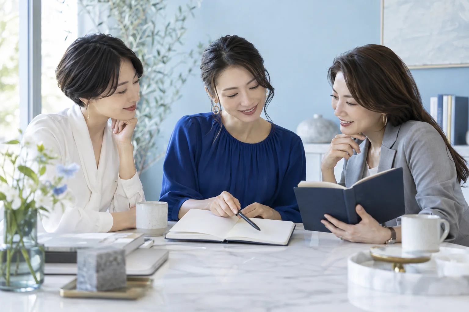本とノートを囲みながら語り合う三人の女性経営者