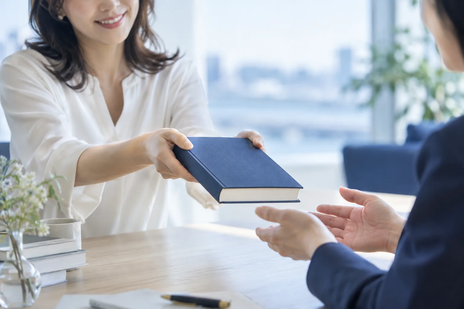 一冊の本を笑顔で相手へ手渡す女性